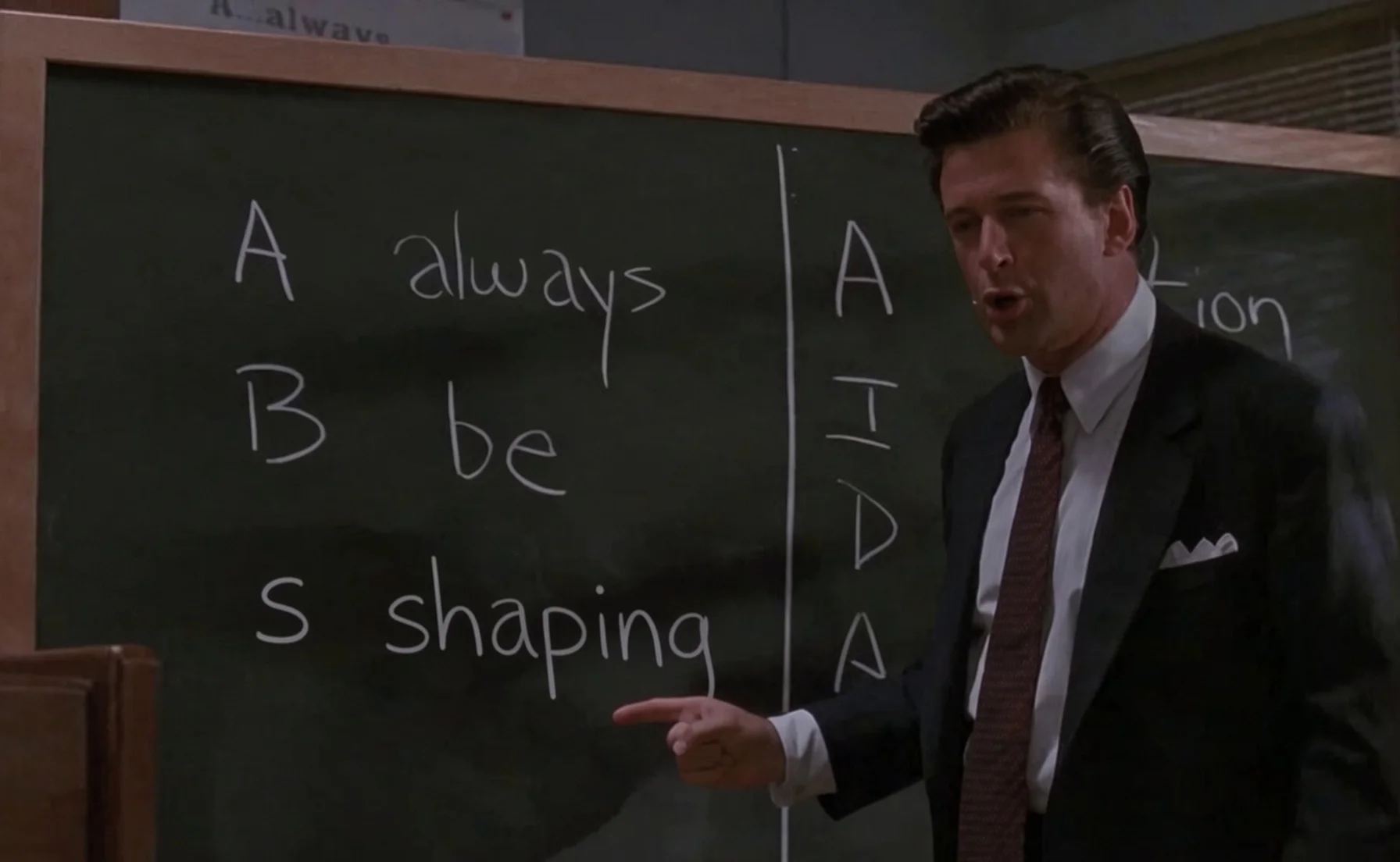 Alec Baldwin in front of a blackboard with "Always Be Shaping" written on it